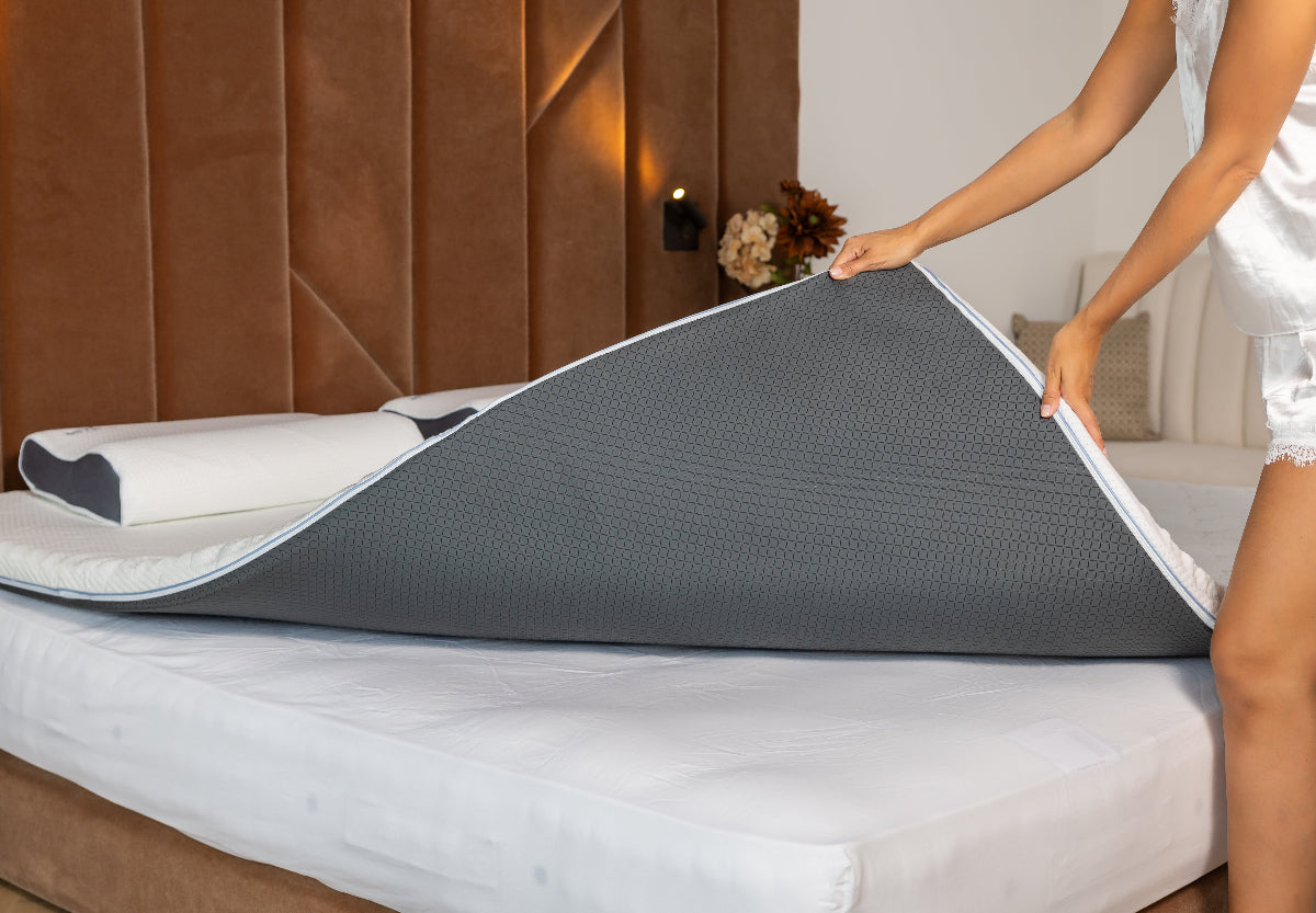 Vrouw legt een Best Life matrastopper met grijze onderkant op het matras