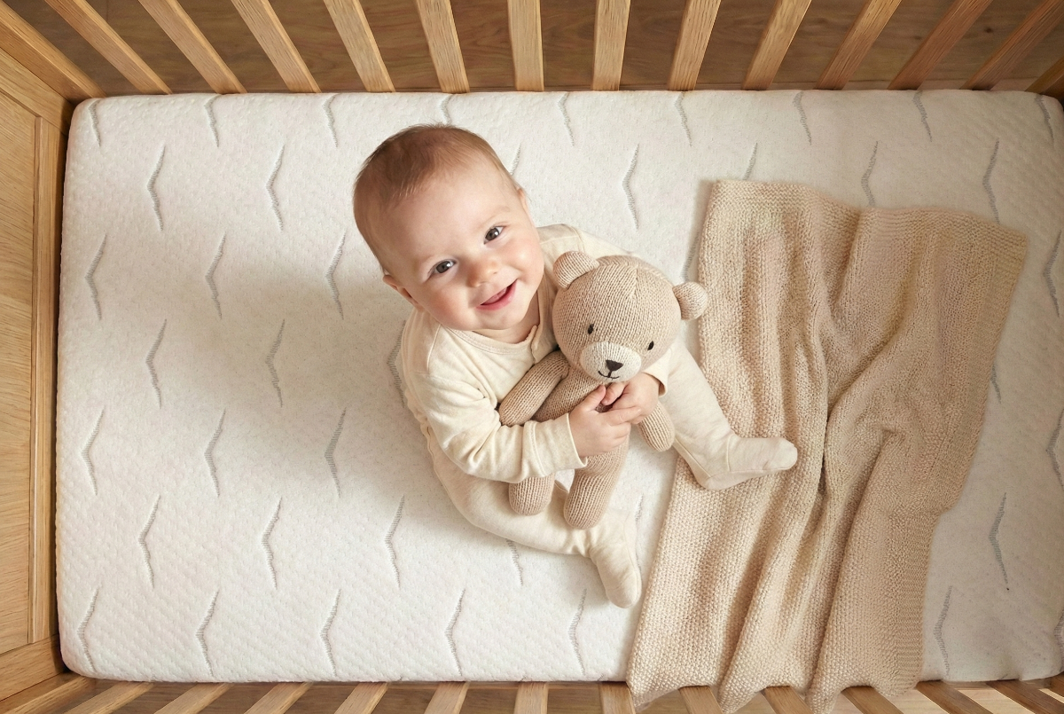 Lachende baby met knuffel op Babymatras Nimba in het ledikant