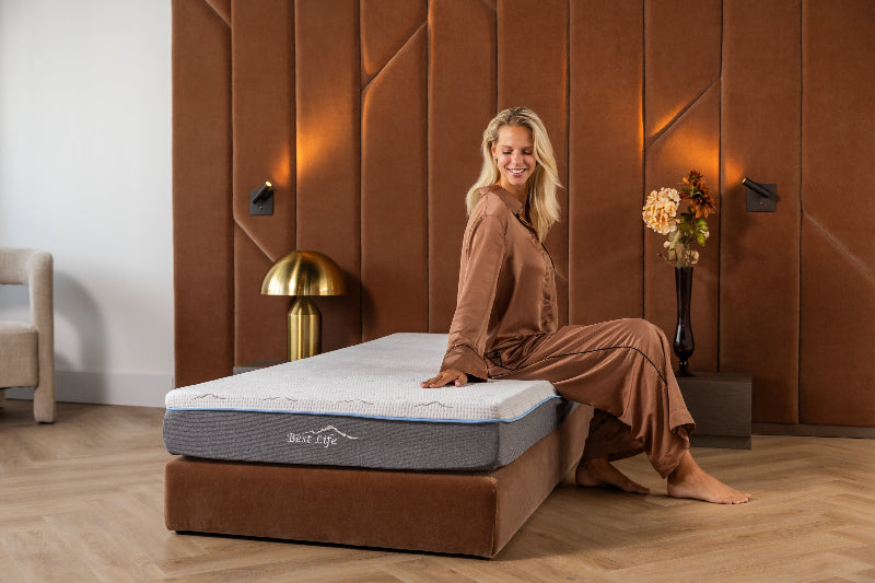 Vrouw zit op de rand van een Best Life matras op een bruin boxspring bed