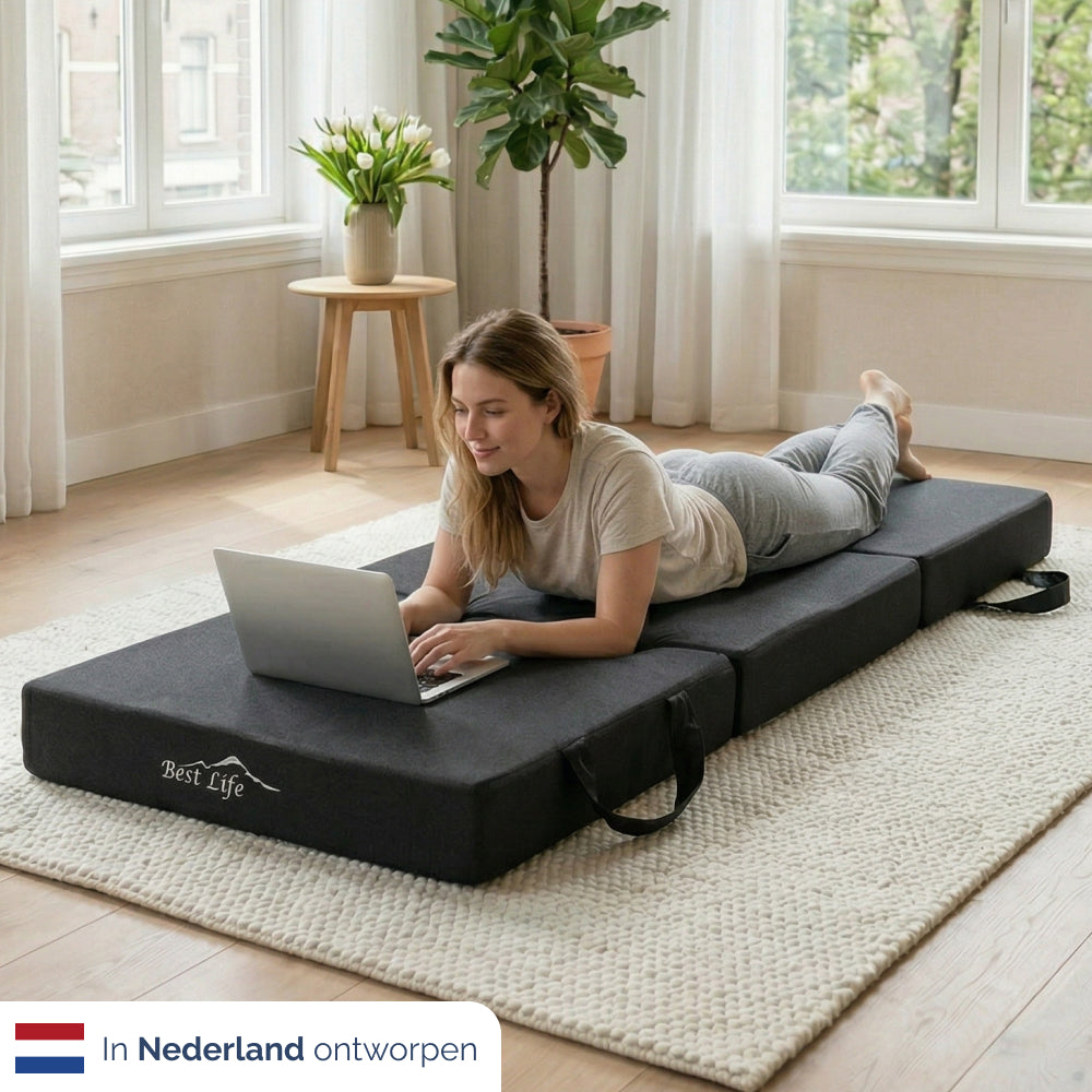 Vrouw ligt met laptop op uitgevouwen Vouwmatras Sella op de vloer
